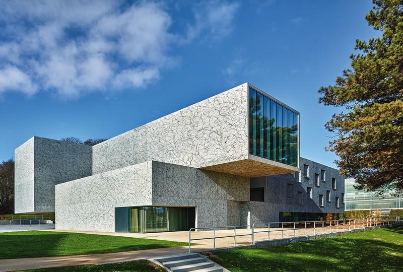 Un monolithe de béton qui affiche une présence énigmatique. le volume de la salle de danse se projette en porte-à-faux vers la citadelle de Belfort.