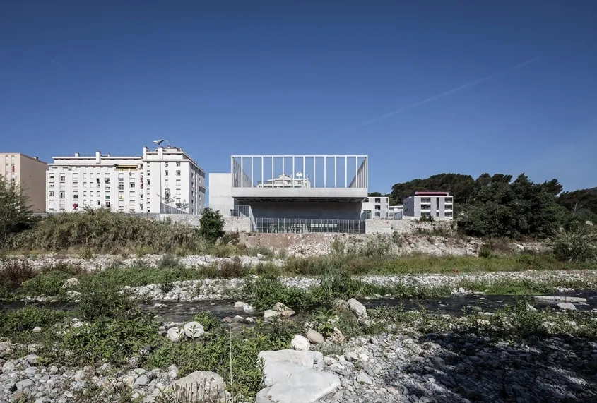 La salle s’implante perpendiculairement au fleuve et s’insère dans son contexte urbain par sa justesse et sa sobriété.