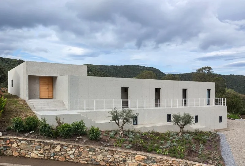 La maison se déploie par un jeu de volumes en béton sablé aménagés dans la pente.