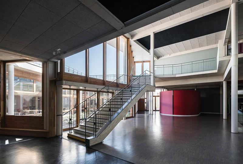 Hall d’accueil éclairé par de grandes baies vitrées donnant sur le patio. l’escalier en béton est suspendu dans la double hauteur.