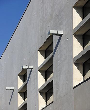 Façade sud, des brise- soleil en béton préfabriqués protègent les ouvertures du rayonnement tout en participant à leur redécoupage. e__ la casquette installée sur la façade arrière, côté stade, fait écho à celle marquant l’entrée principale dans le gymnase. f __ sur la façade arrière, côté buvette, gradins et rampe font le lien avec le stade existant. g __ f outre leur intérêt graphique, les leds insérées dans les trous de banche participent au rôle de signal du bâtiment.