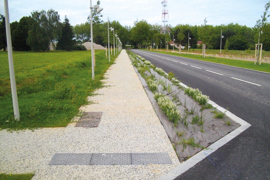 La voie cyclable étant partagée avec des piétons,  des dalles podotactiles ont été installées pour guider  les personnes à mobilité réduite. Les bordures de trottoirs  en béton extrudé (profil CS1) permettent l’écoulement des eaux pluviales dans les noues végétalisées (et ici bâchées).