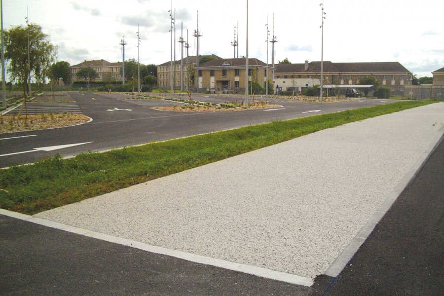 Vue sur les parkings avec, en arrière-plan, les derniers locaux occupés par l’armée de l’air. Au premier plan : le cheminement piéton en béton désactivé qui dessert l’ensemble du complexe. Il débute au niveau de l’arrêt de bus, situé à droite.