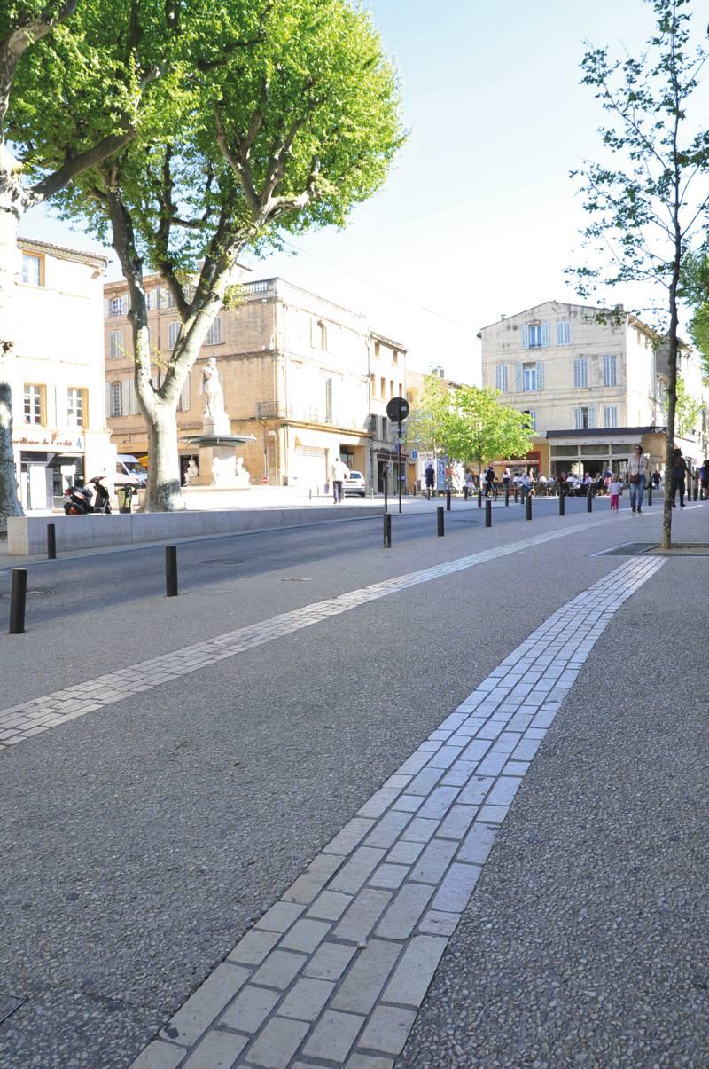 Les cours ont reçu un revêtement de béton désactivé avec des cailloux concassés clairs et un calepinage de bandes structurantes en pierres calcaires naturelles Cénia.