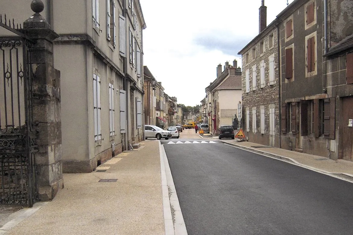 Au premier plan, la route de Beaune avec ses trottoirs en béton désactivé.  Au second plan, la rue de la République en béton désactivé coloré sur chaussée et en béton bouchardé sur les parkings.